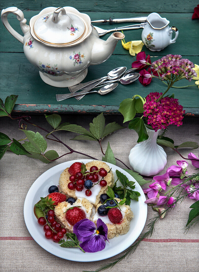 Teegebäck dekoriert mit Beeren und Blüten auf rustikalem Holztisch