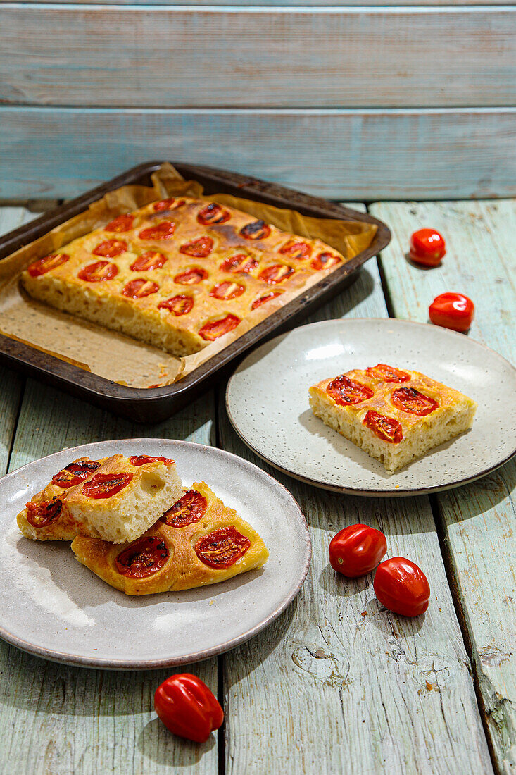 Tomato focaccia on a baking tray and pieces on plates