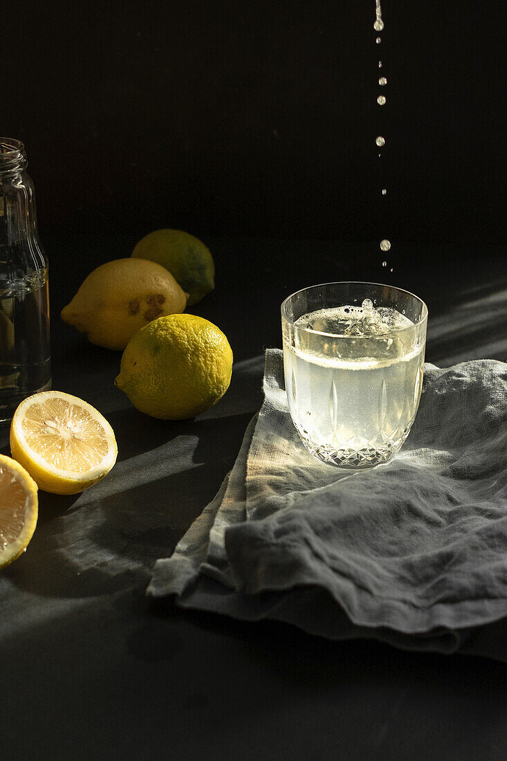 Frisch gepresster Zitronensaft tropft in ein Glas Wasser