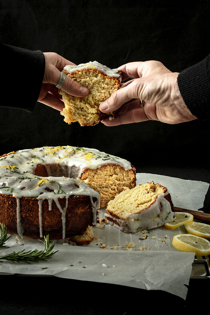 Veganer Zitronen-Kranzkuchen mit Rosmarin, zwei Hände greifen nach Kuchenstück