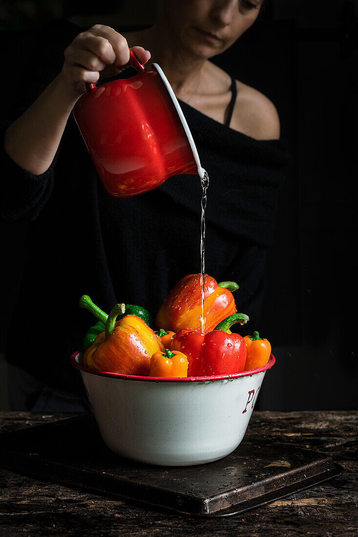 Woman pouring water over red and yellow peppers
