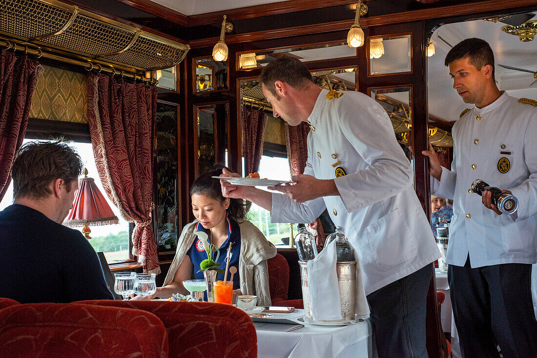 Ein Kellner serviert das Mittagessen im Art-Deco-Restaurantwagen des Luxuszuges Belmond Venice Simplon Orient Express. Lachskraut und Kartoffeln
