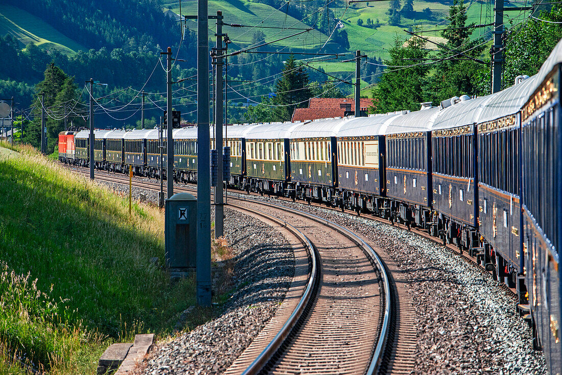 Train running along villages of Dolomites scenery. Belmond Venice Simplon Orient Express luxury train.
