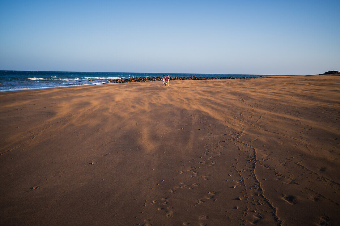 Couple walks on the beach as a strong wind blows sand in Lanzarote, Canary Islands, Spain