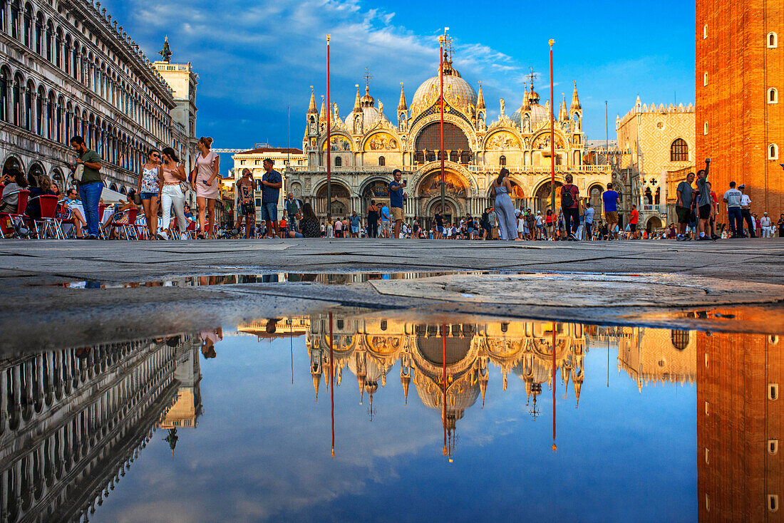 Basilica San Marco reflected in acqua alta in Piazza San Marco at twilight during sunset, Venice, Italy with motion blur on the crowds of tourists