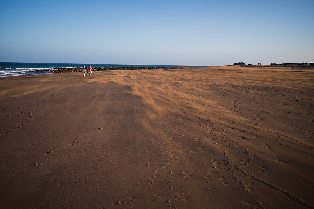 Ein Paar geht am Strand spazieren, während ein starker Wind den Sand auf Lanzarote, Kanarische Inseln, Spanien, verweht