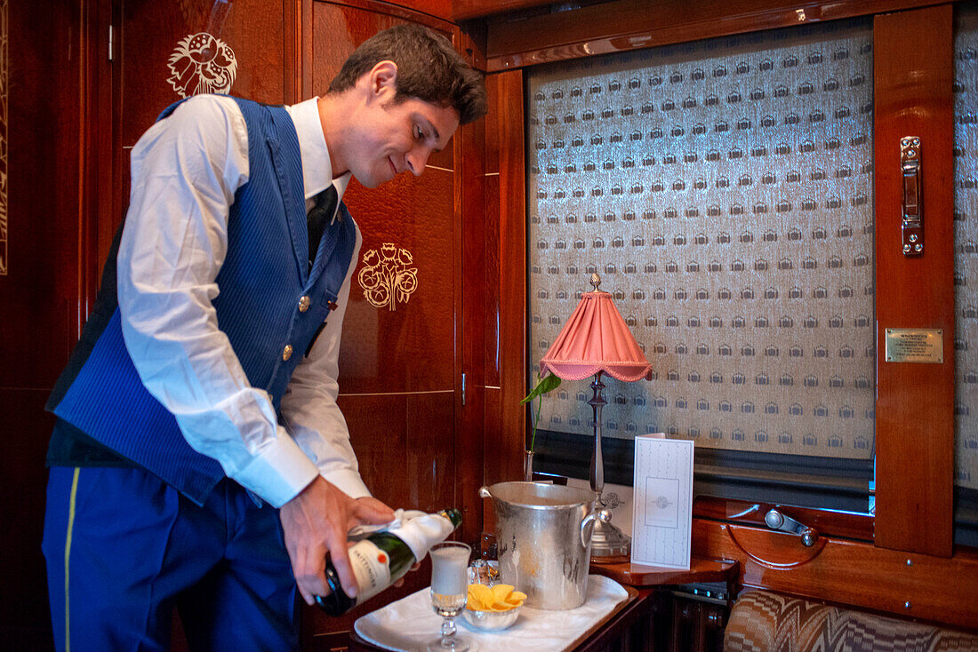Ein Kellner serviert Champagner in einem der Einzelabteile des Luxuszuges Belmond Venice Simplon Orient Express