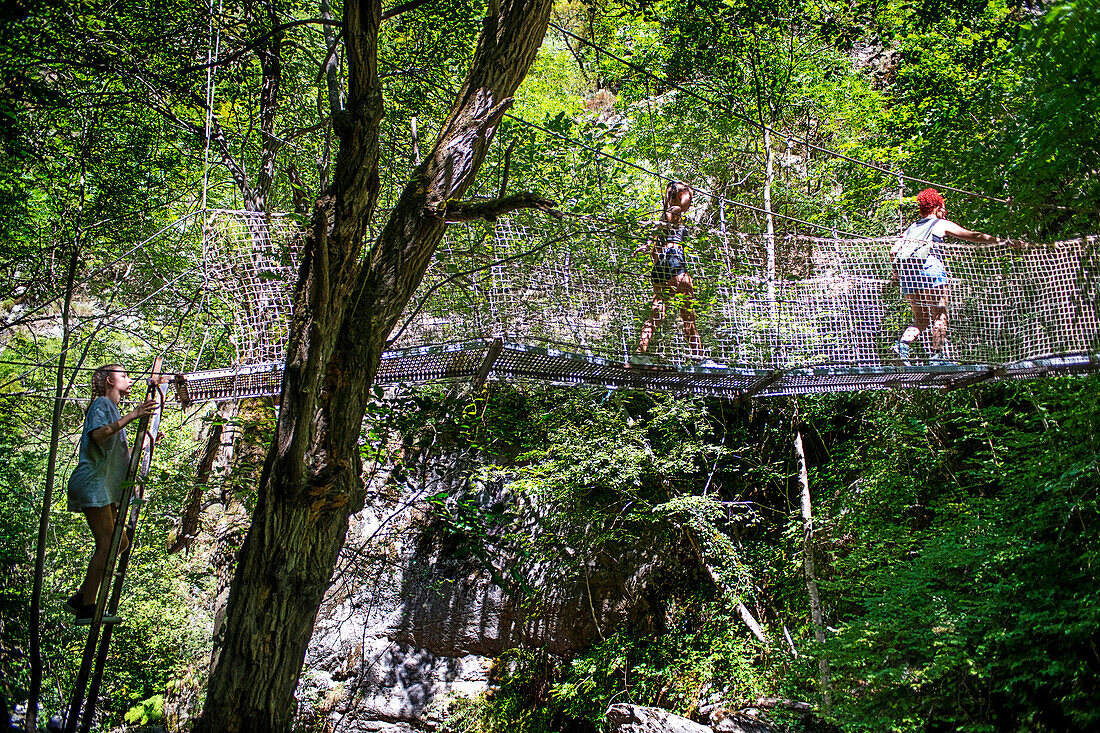 Hiker crossing metal suspension bridge on hiking trail through Gorges de la Carança, Pyrénées-Orientales, Languedoc-Roussillon, France.