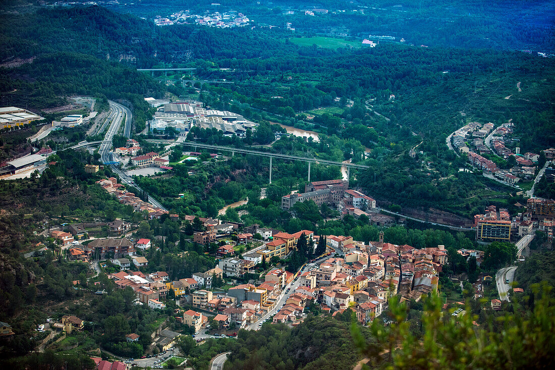 Luftaufnahme der Stadt Monistrol de Montserrat von der Cremallera de Montserrat aus, der Zahnradbahn, die die Stadt mit dem Kloster Montserrat (Monasterio de Montserrat) im Gebirgsmassiv bei Barcelona, Katalonien, Spanien, verbindet. In der Mitte ist die Überführung der Zahnradbahn zu sehen, links der Bahnhof.