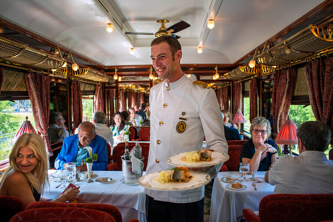 A waiter serves the dinner inside the art deco restaurant wagon of the train Belmond Venice Simplon Orient Express luxury train. Salmon cabbage and potatoes
