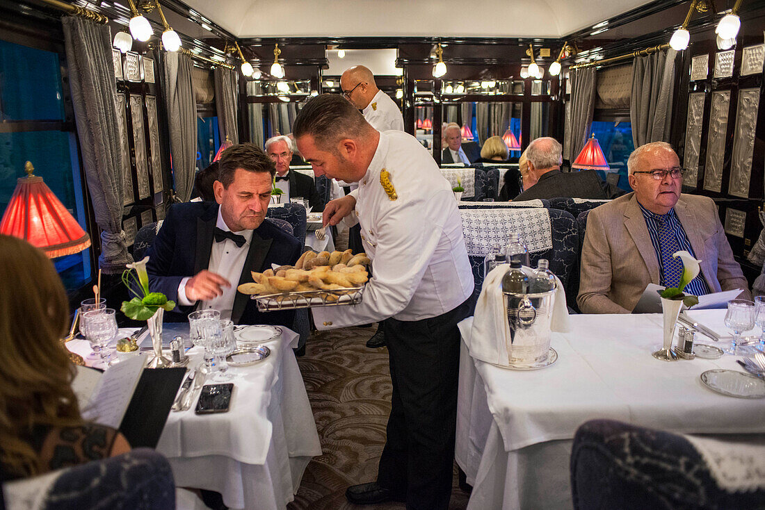 A waiter serves dinner in the art deco restaurant wagon of the train Belmond Venice Simplon Orient Express luxury train.