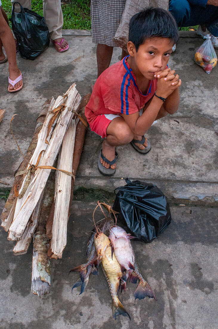 Ein Junge verkauft Brennholz und Fisch auf dem Markt in Indiana viallage, Iquitos, Loreto, Peru