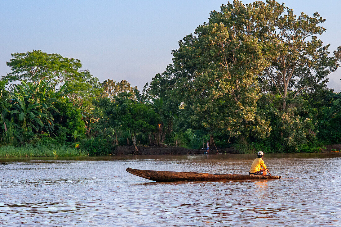 Kleines Holzboot mit Einheimischen auf dem Purus-Fluss im Amazonasgebiet an einem sonnigen Sommertag mit Bäumen am Flussufer, in der Nähe von Iquitos, Loreto, Peru. Fahrt auf einem der Nebenflüsse des Amazonas nach Iquitos, etwa 40 Kilometer von der Stadt Indiana entfernt