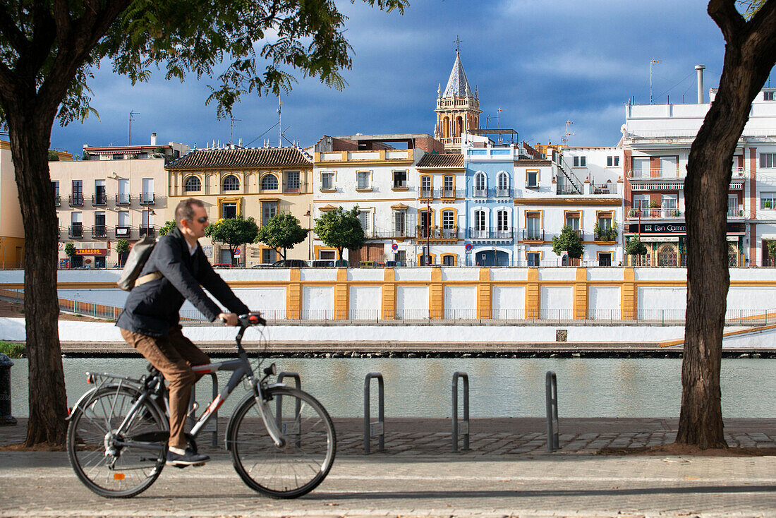 Radfahrer fahren am Ufer des Flusses Guadalquivir entlang. Rückansicht von Häusern und Wohnungen im Stadtviertel Triana in Sevilla - Sevilla