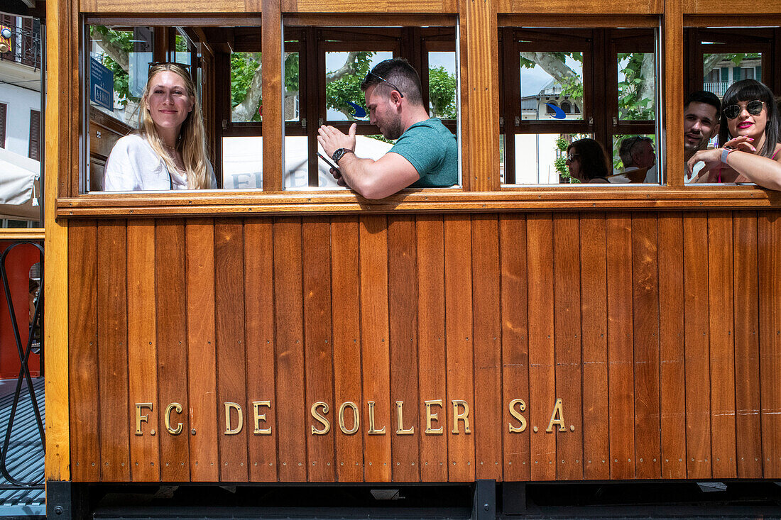 Touristen in der historischen Straßenbahn im Dorfzentrum von Soller. Die Straßenbahn verkehrt auf einer Strecke von 5 km zwischen dem Bahnhof im Dorf Soller und dem Puerto de Soller, Soller Mallorca, Balearen, Spanien, Mittelmeer, Europa