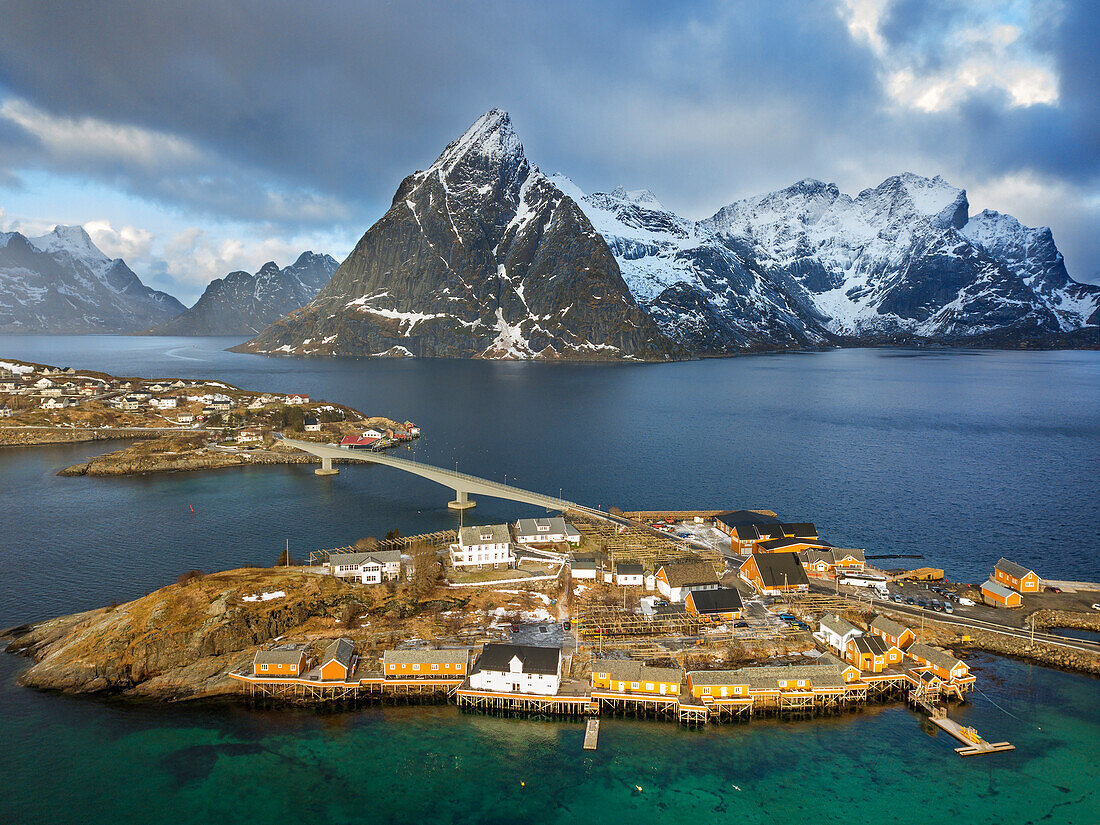 Luftaufnahme der traditionellen Holzhütten der Rorbu-Fischer im Dorf Sakrisoy auf der Insel Moskenesoya auf den Lofoten in Norwegen. Landschaft mit dem Berg Olstinden