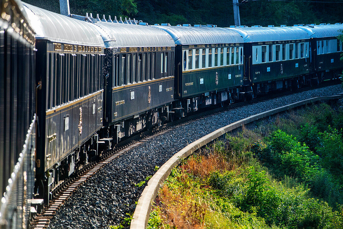 Train running along villages of Dolomites scenery. Belmond Venice Simplon Orient Express luxury train.