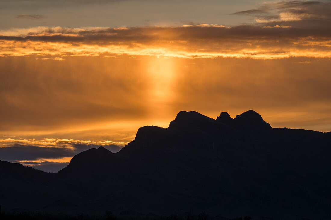 Eine Sonnensäule bei Sonnenaufgang über den Bergen, verursacht durch Licht, das von Eiskristallen in der Atmosphäre reflektiert wird. Quartzsite, Arizona