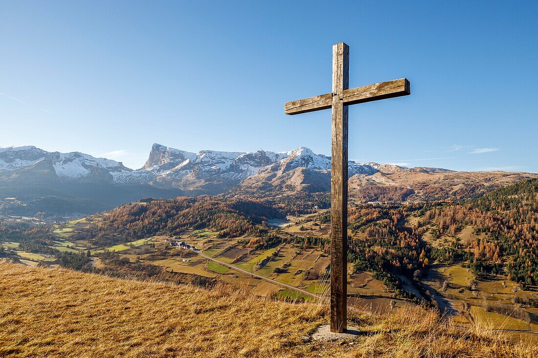 Frankreich, Hautes Alpes, Dévoluy-Massiv, Holzkreuz oberhalb des Dorfes Saint Etienne en Dévoluy, im Hintergrund die Station SuperDévoluy, das Plateau und der Gipfel des Bure (2709m)