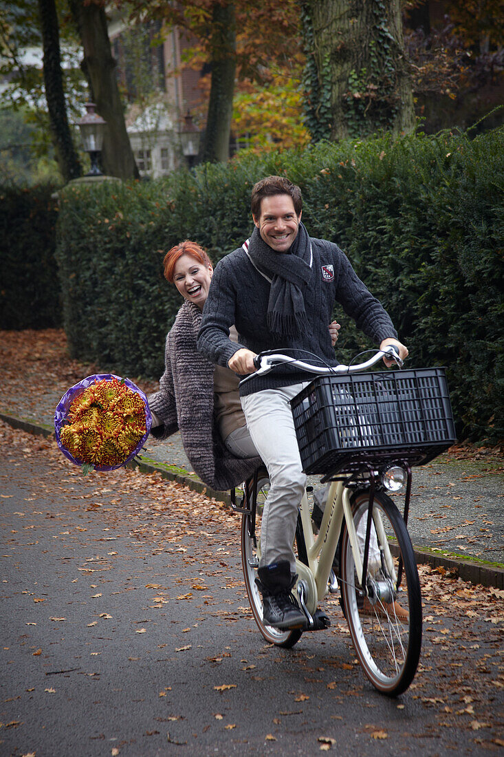 Fahrradfahrendes Paar mit Blumen in der Hand