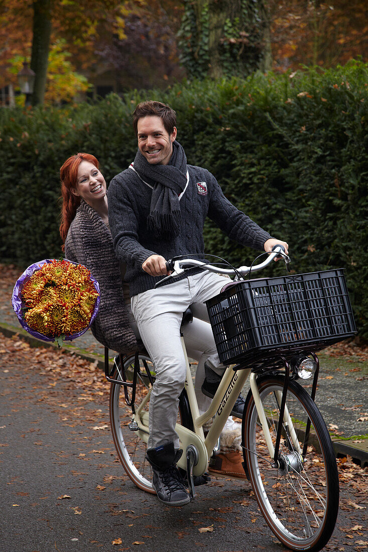 Couple riding bicycle holding flowers