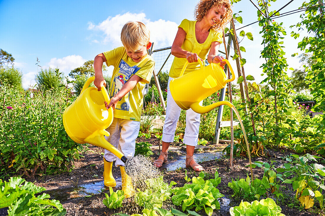 Boy and mother watering vegetable beds