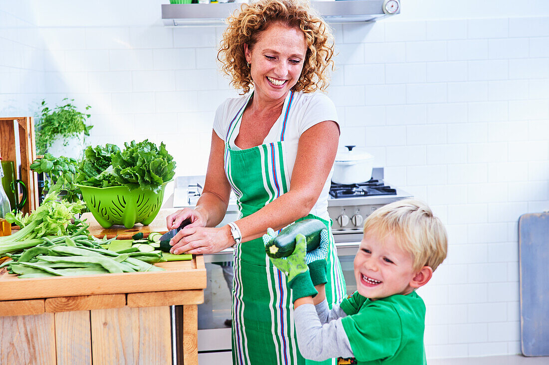 Woman cutting green vegetables and salad with her son, kitchen