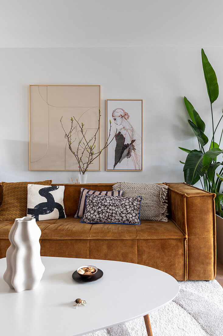 Brown corner sofa in front of a white wall with framed artwork and large indoor plants