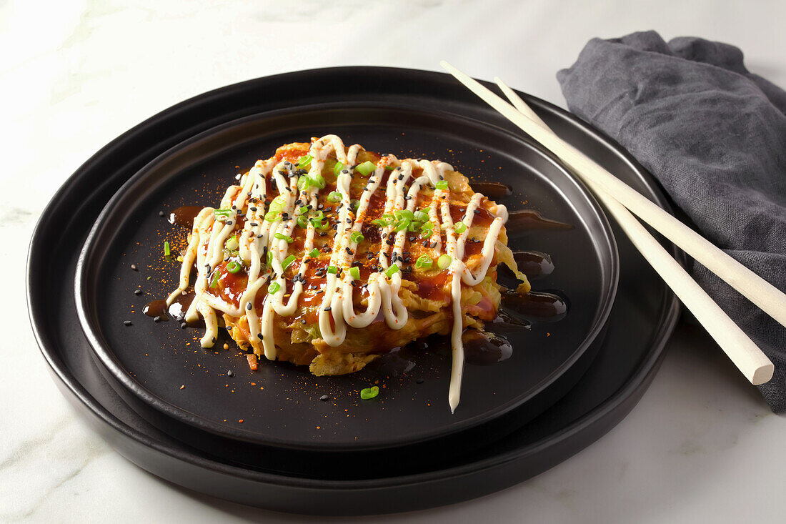 Okonomiyaki-Omelett nach japanischer Art, garniert mit Okonomi-Sauce, japanischer Mayonnaise und Frühlingszwiebeln