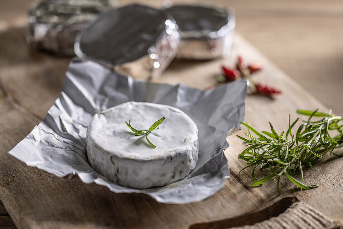 Brie cheese in aluminium foil with rosemary and chilli on a chopping board