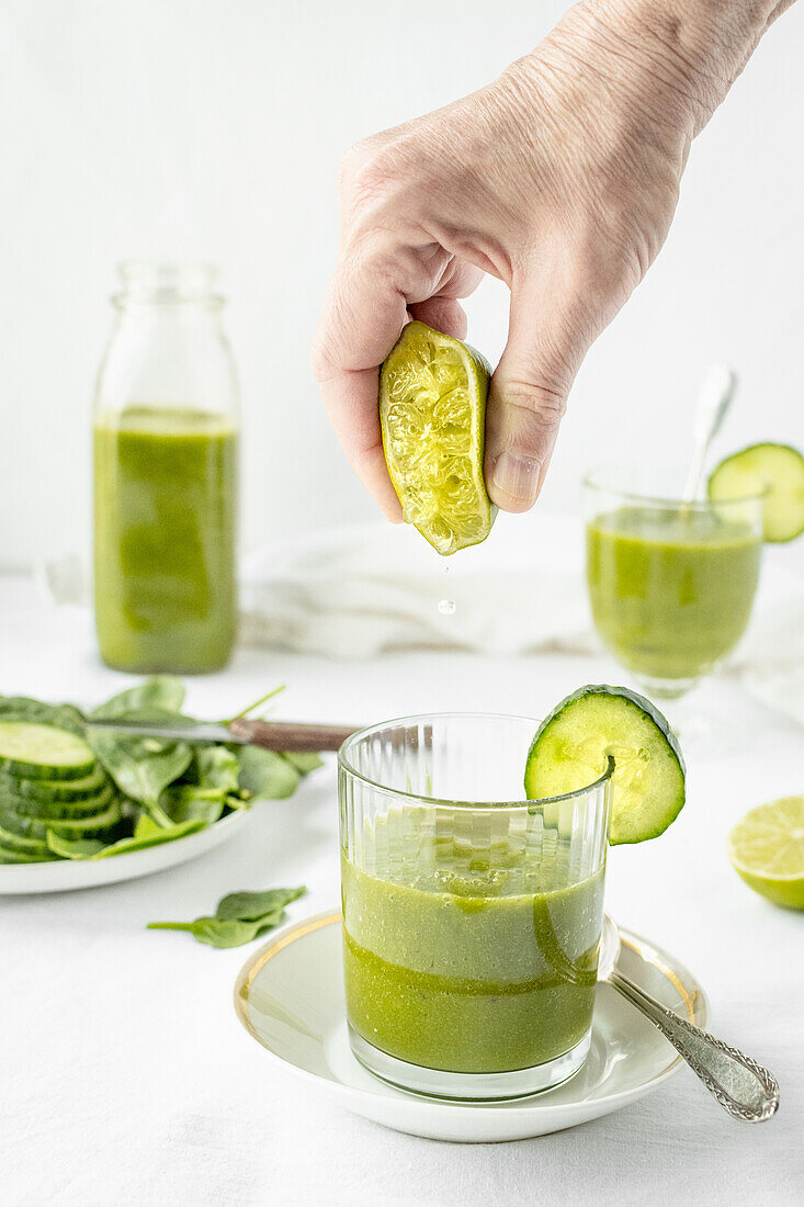 Hand presst Limette in grünen Smoothie aus Gurken und Spinat