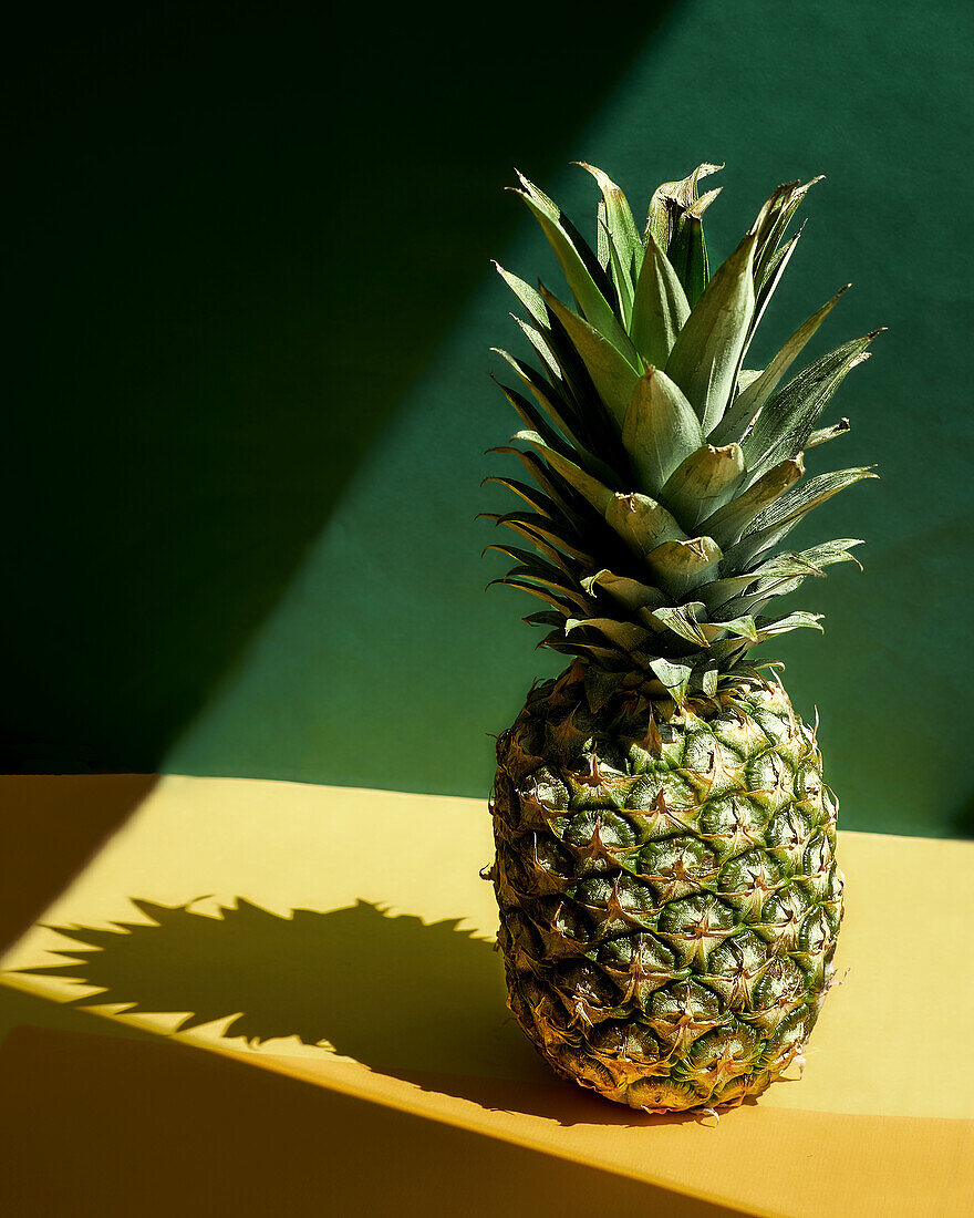 Whole pineapple against a yellow and green background in the sunlight