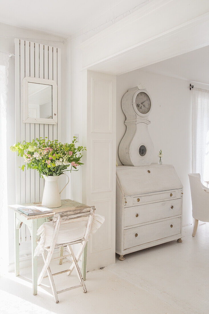 White country house furniture in a light-coloured room with a bouquet of flowers in a vase