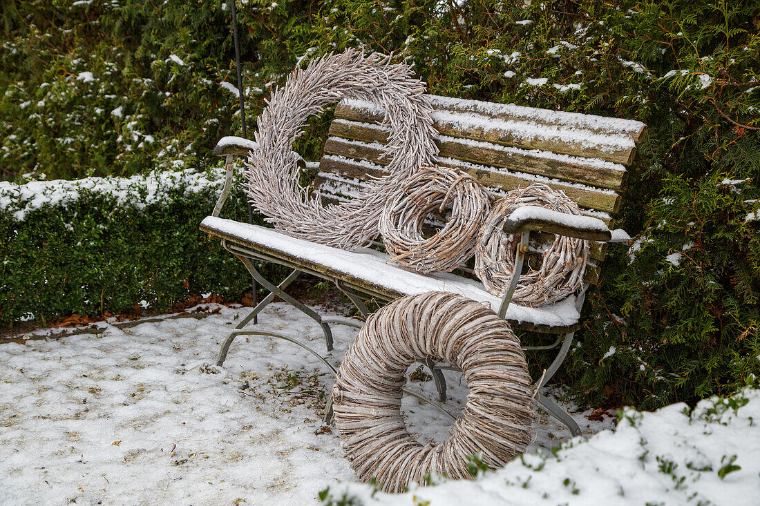 Schneebedeckte Gartenbank mit dekorativen Kränzen im Winter