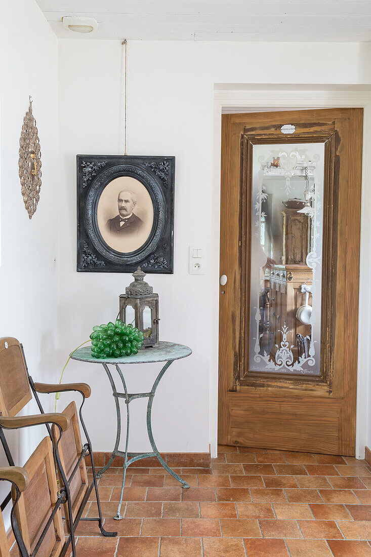 Eingangsbereich mit antiken Holzstühlen, Metalltisch und historischem Portraitfoto an der Wand