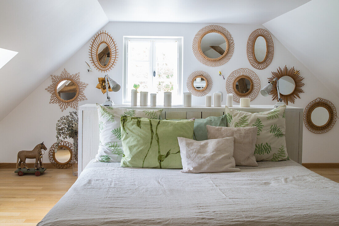 Schlafzimmer mit Dachschräge, weiß-grüner Bettwäsche und Rattan-Spiegeln an der Wand