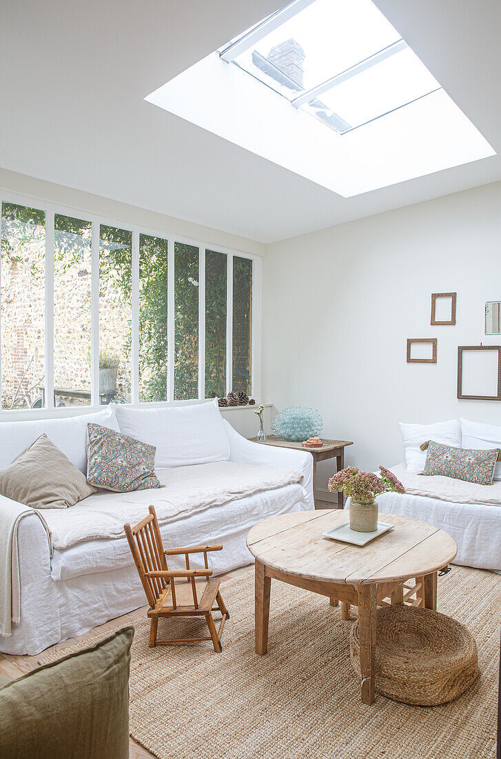 Bright living room with skylight, white sofas and wooden furniture