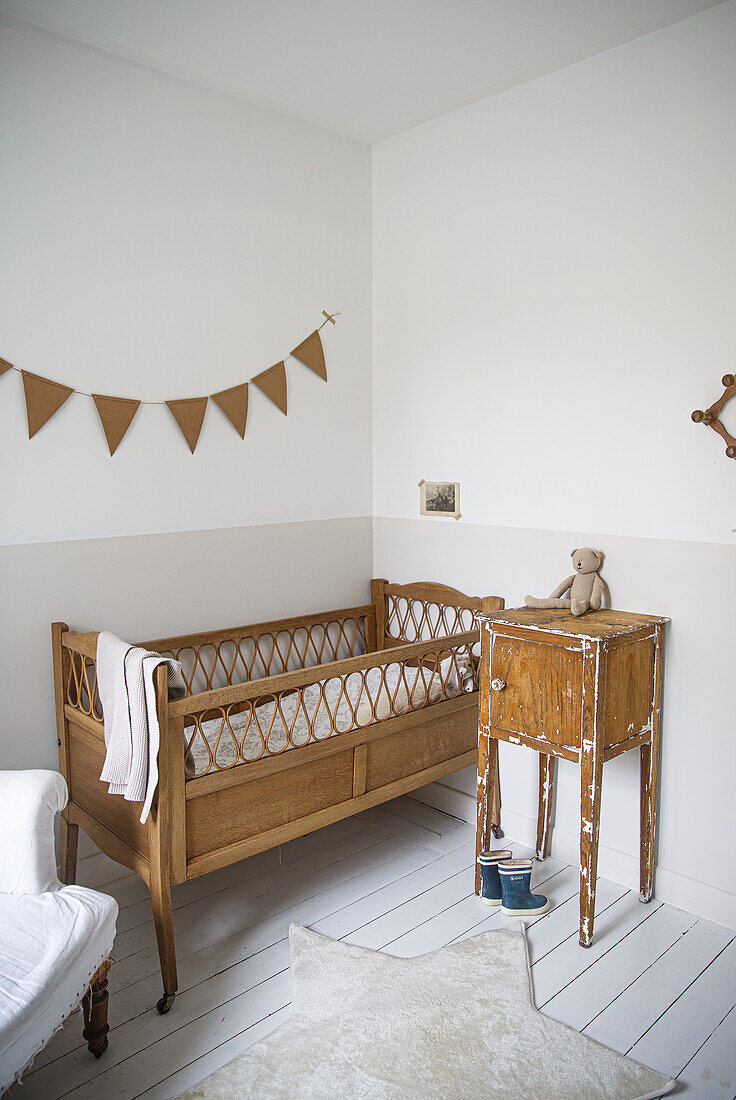 Baby room with wooden cot, vintage bedside table and bunting on the wall