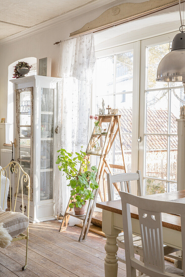 Country-style dining room with ladder shelf and plants in front of floor-to-ceiling windows