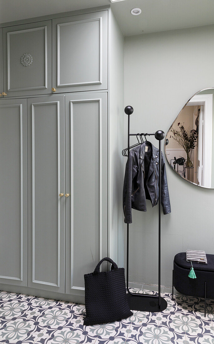 Entrance area with pastel green fitted wardrobes, leather jacket on coat rack and bag on patterned tiled floor