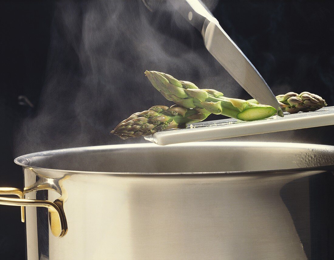 Grüne Spargelspitzen kommen in einen dampfenden Kochtopf