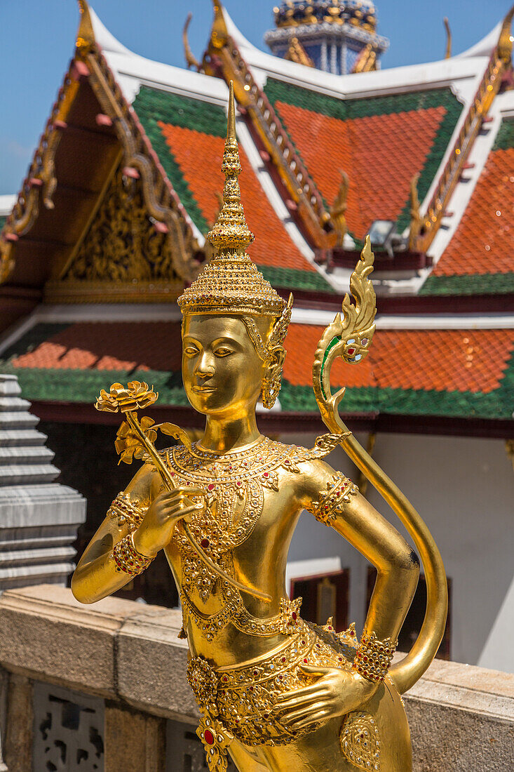 Golden statue of a mythical Thepnorasi guards the Temple of the Emerald Buddha in the Grand Palace complex in Bangkok, Thailand.