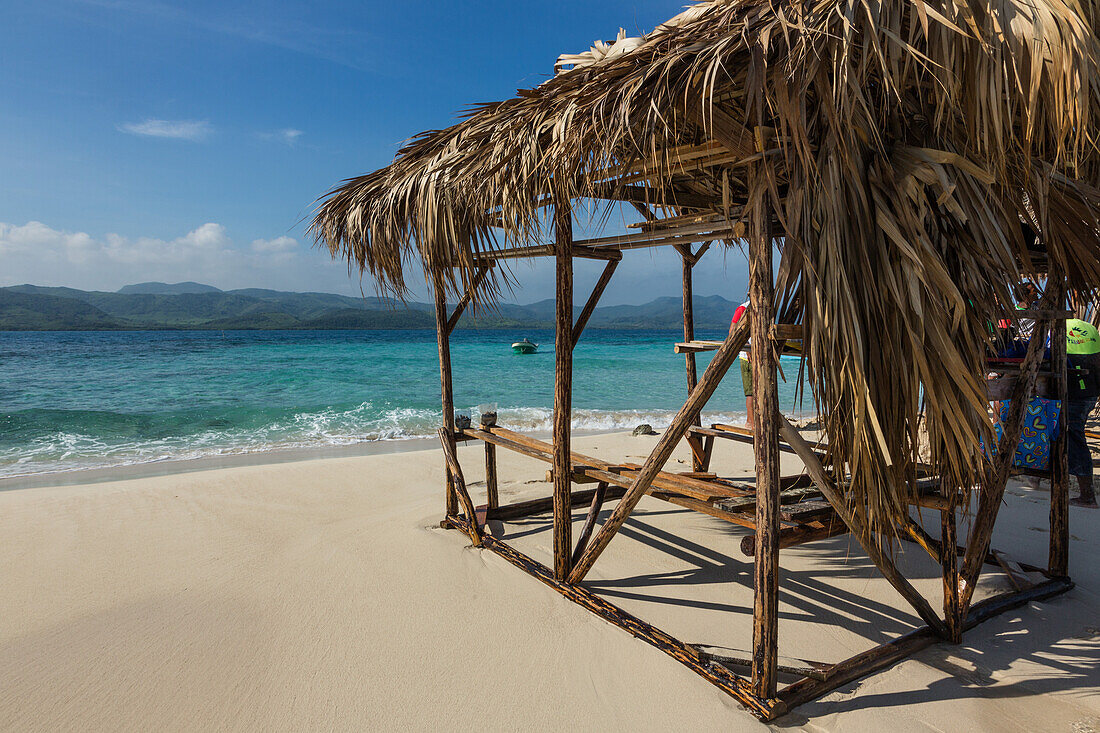 A thatched-roofed shelter on Cayo Arena or Paradise Island. In the background is Monte Cristi National Park in the Dominican Republic., Hispaniola.