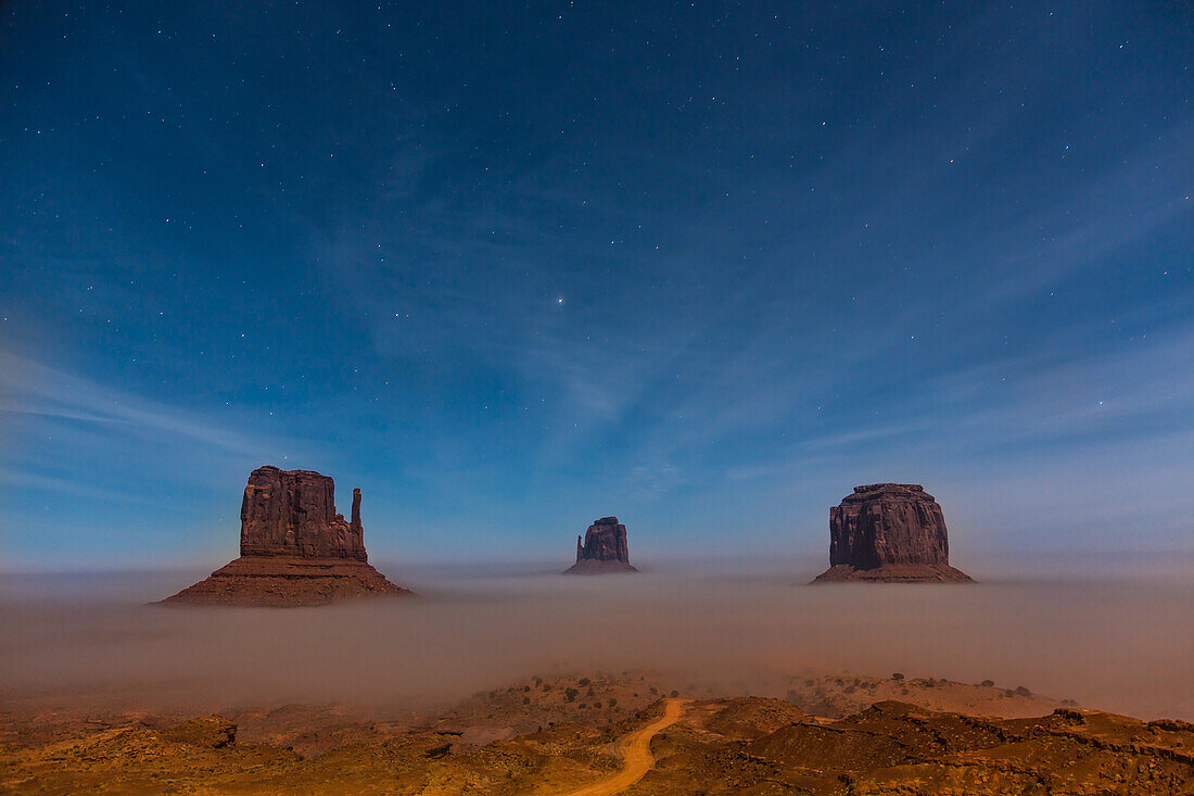 Ground fog at the base of the Mittens at night with stars overhead in the Monument Valley Navajo Tribal Park in Arizona.