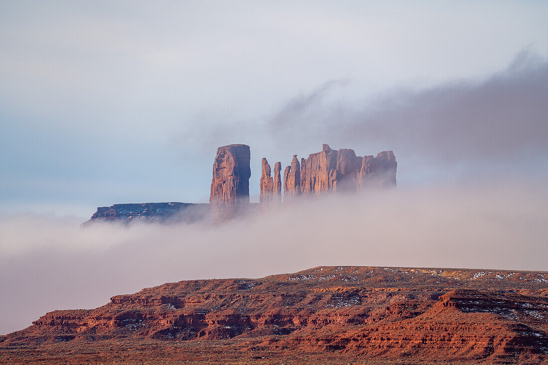 Niedrige Wolken um die Castle Butte, den Bear and the Rabbit und die Stagecoach im Monument Valley Navajo Tribal Park in Arizona. Diese Monumente werden oft als Utah Monuments bezeichnet, weil sie sich direkt hinter der Grenze in Utah befinden, während der größte Teil des Parks in Arizona liegt.