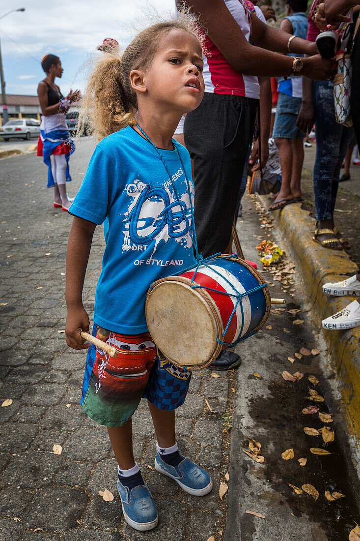 Ein kleines dominikanisches Mädchen mit ihrer Tambura-Trommel wartet auf den Jugendkarnevalsumzug in Santo Domingo, Dominikanische Republik