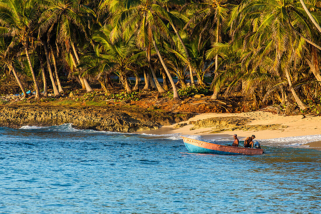 Two fishermen prepare to launch their boat in the early morning in the Bay of Samana, near Samana, Dominican Republic. Palm trees line the shore.