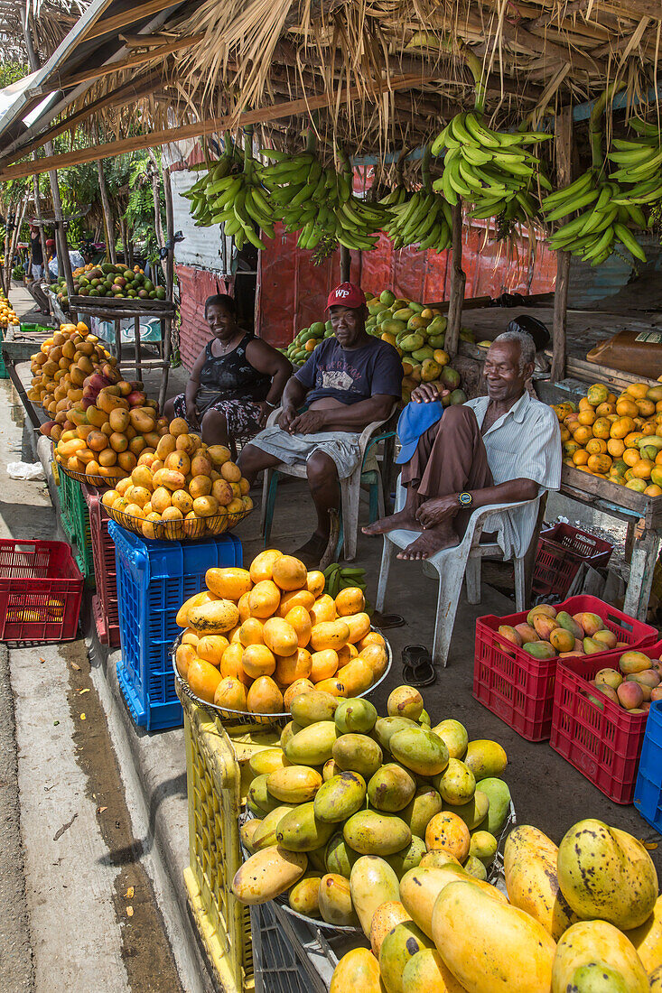 Drei Personen verkaufen Mangos an einem Obststand am Straßenrand in Bani, Dominikanische Republik