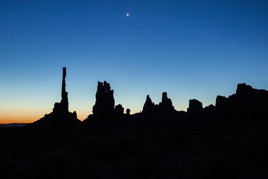 Stars over the Totem Pole and the Yei Bi Chei in silhouette before dawn in the Monument Valley Navajo Tribal Park in Arizona.