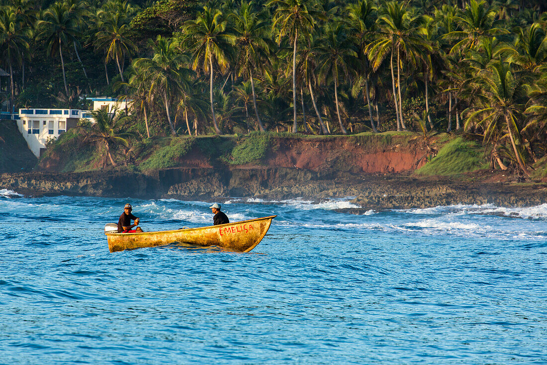 Zwei Fischer in ihrem kleinen Boot in der Bucht von Samana, nahe Samana, Dominikanische Republik. Palmen säumen das Ufer